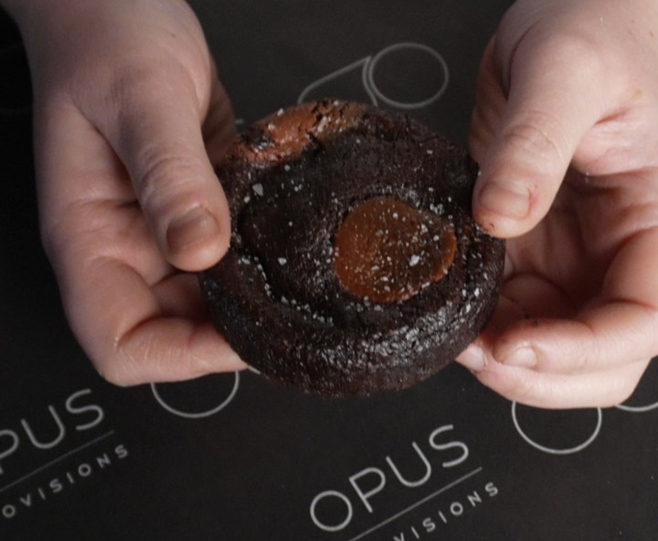 Oven-ready chocolate cookie held over branded Opus paper