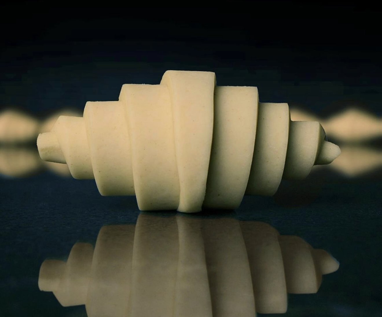 Hand-rolled croissant, proof-and-bake, on a dark reflective surface