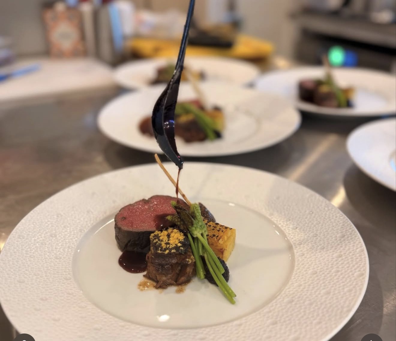 Venison loin being sauced on a white plate during service